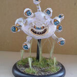 Whimsical white many-eyed monster sculpture on a grassy black base.