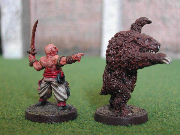 Two fantasy miniatures on grass: a sword-wielding man faces a furry monster.