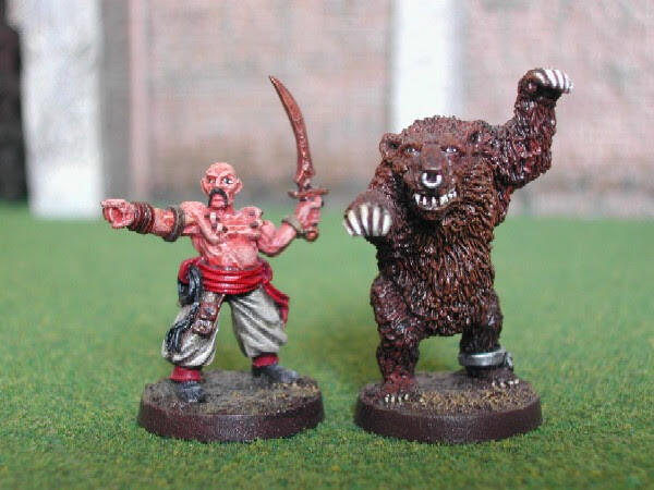 Two painted miniatures on green turf: a red warrior and a larger brown beast.