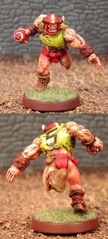 Front and back views of a painted red-and-gold monster miniature on a green base.